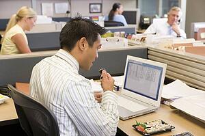 Businessman in cubicle at laptop eating sushi