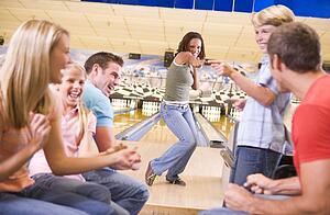 Family in bowling alley with two friends cheering and smiling