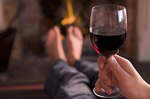 Feet warming at fireplace with hand holding wine
