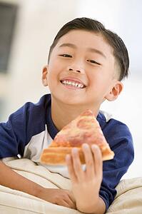 Young boy eating pizza slice in living room smiling