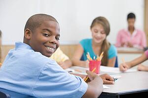 Students in class writing with teacher in background (selective focus)