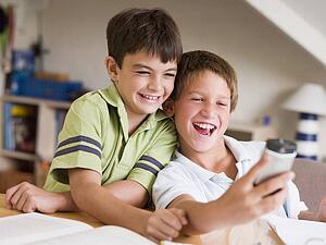 Two Young Boys Distracted From Their Homework, Playing With A Cellphone