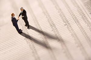 Figurines Of Two Businessmen Shaking Hands On A Financial Newspaper