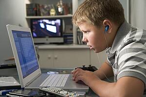 Young boy in bedroom using laptop and listening to MP3 player