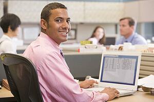 Businessman in cubicle with laptop smiling