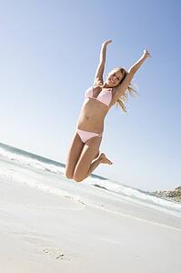 Woman in a two piece bathing suit jumping on a beach