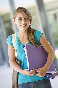 Student standing outside school with binder smiling (selective focus)