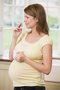 Pregnant woman standing in kitchen with coffee and cigarette