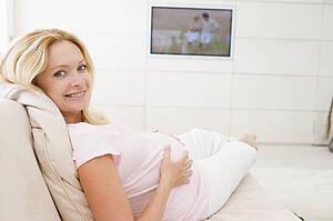 Pregnant woman watching television smiling