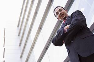 Businessman standing outdoors by building smiling (high key/selective focus)