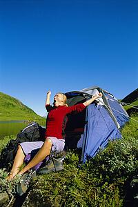 Woman outdoors at campsite by lake yawning and stretching