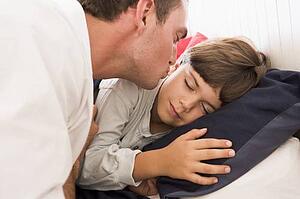 Man waking young boy in bed with kiss