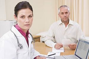 Doctor with laptop and man in doctor's office frowning