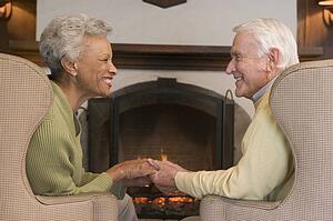 Couple sitting in living room by fireplace holding hands and smiling