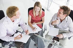 Three businesspeople in a boardroom looking at paperwork
