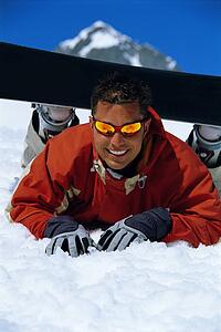 Snowboarder lying on snowy hill wearing board and smiling (selective focus)