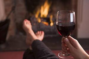 Feet warming at fireplace with hand holding wine
