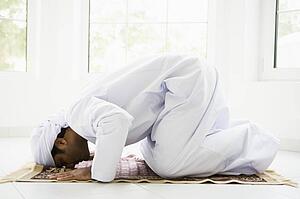 Man indoors praying on mat (high key)