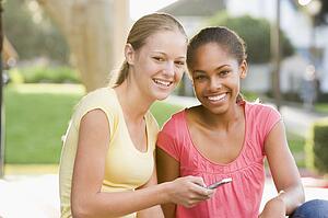 Teenage Girls Sitting Outside Playing With Mobile Phone
