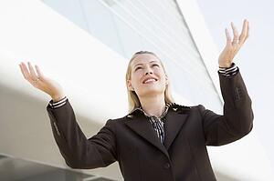 Businesswoman standing outdoors by building with hands out smiling