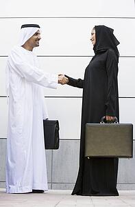 Two businesspeople standing outdoors with briefcases shaking hands and smiling