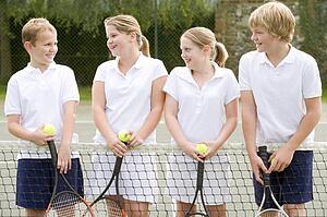 Four young friends with rackets on tennis court smiling