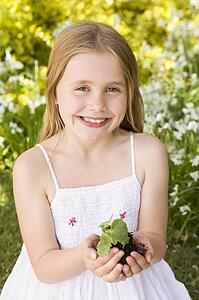 Young girl outdoors holding plant smiling