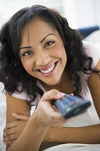 Woman in living room holding remote control smiling (high key/selective focus)
