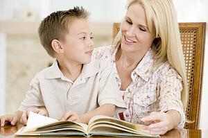 Woman and young boy reading book in dining room smiling