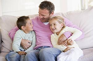 Man and two children sitting in living room smiling