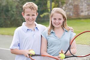 Two young friends with rackets on tennis court smiling