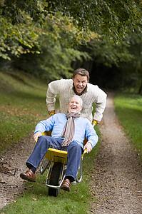 Son pushing senior father in wheelbarrow