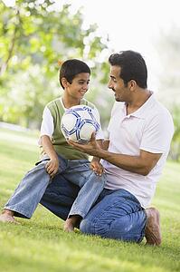 Father and son outdoors in park with ball smiling (selective focus)