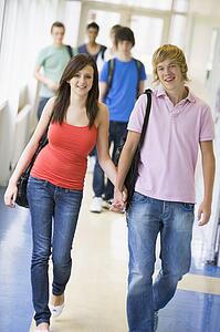 Two students walking in corridor holding hands with students in background (selective focus)