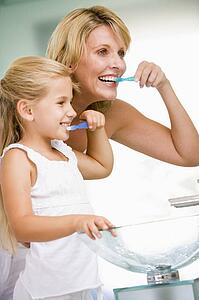 Woman and young girl in bathroom brushing teeth