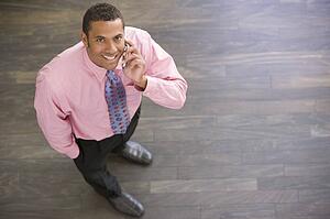 Businessman standing indoors using cellular phone smiling