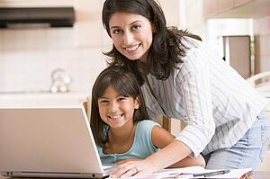 Woman and young girl in kitchen with laptop and paperwork smiling
