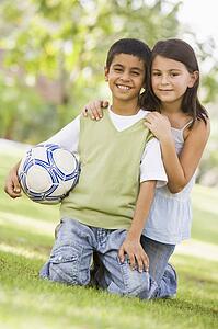 Two young children outdoors in park with ball smiling (selective focus)