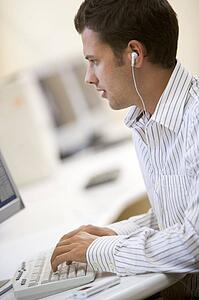 Man in computer room listening to MP3 player while typing