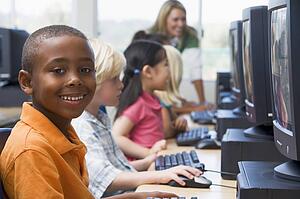 Children at computer terminals with teacher in background (depth of field/high key)