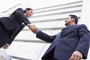 Two businesspeople outdoors by building shaking hands and smiling (high key/selective focus)