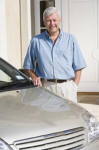 Senior man standing with his car outside his home