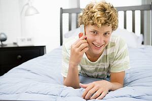 Teenage Boy Lying On Bed Using Mobile Phone 