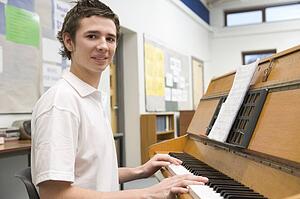 Male student learning piano in classroom