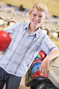 Young boy in bowling alley holding ball and smiling