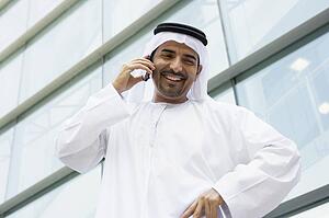 Businessman standing outdoors by building on cellular phone smiling (selective focus)