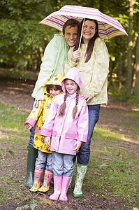 Family outdoors in rain with umbrella smiling