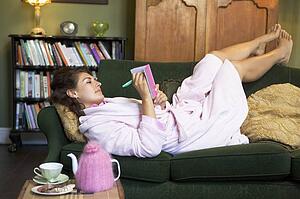 Young woman lying on sofa at home writing in her diary