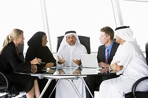 Five businesspeople in office with laptop talking and smiling (high key/selective focus)
