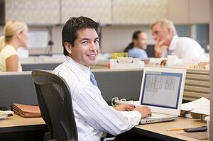 Businessman in cubicle with laptop smiling